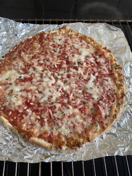 Picture of a pizza margherita bought frozen all ready to be served sitting on a piece of aluminum foil in the oven