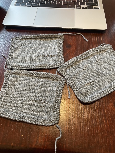 Three knitted gauge swatches in stockinette stitch from a light gray, marled yarn on a table with a laptop sitting behind them
