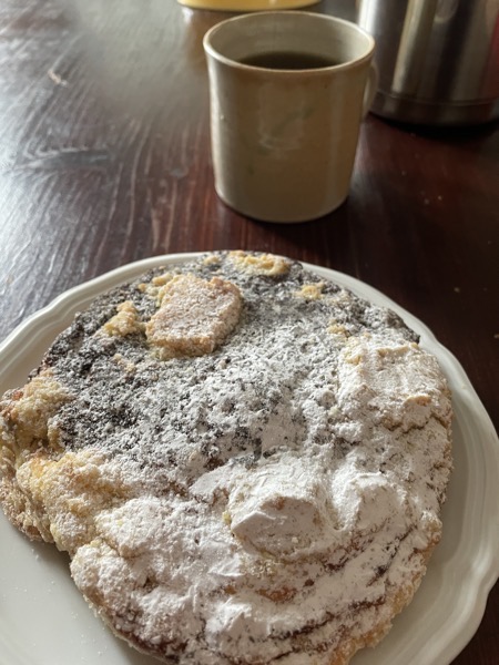 Big pastry with quark, poppy seeds and lots of powdered sugar next to a ceramic mug holding mint tea