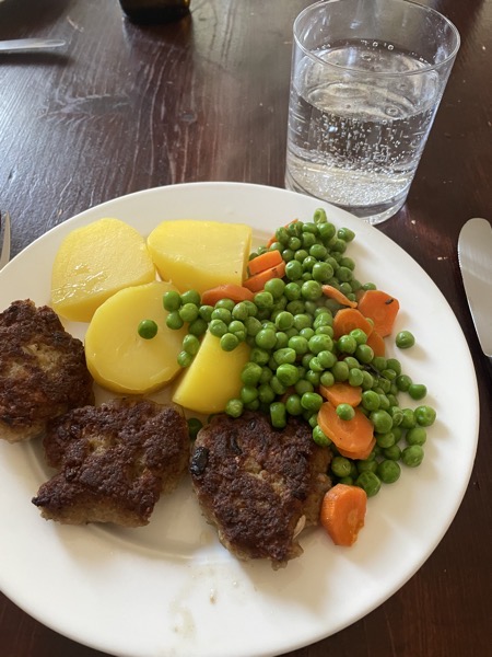 a plate of hamburgers, potatoes, peas and carrots, glass of water