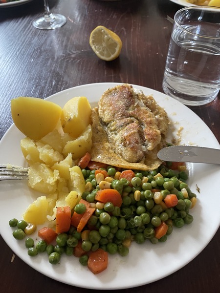 A plate with potatoes, peas and carrots and some breaded fish. Glass of water on the side