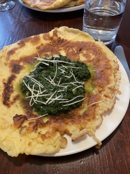 a plate with a pancake with some spinach and parmesan, glass of water on the side