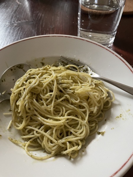 a plate of messy spaghetti and pesto with a glass of water on the side 