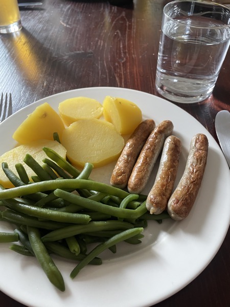 a plate of bratwurst, green beans and potatoes, a glass of water on the side