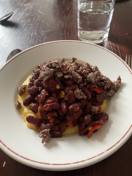 a plate of polenta topped with red beans, veggies and ground beed with a glass of water on the side