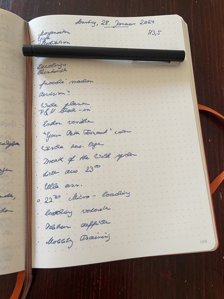 an open orange Leuchtturm 1917 notebook with a very long to-do list written in dark blue ink in German with the pen covering an item of the list