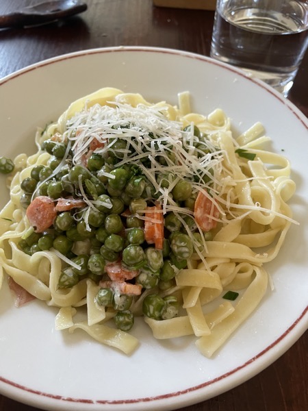 a big portion of tagliatelle with cream sauce, peas, carrots, ham and parmesan with a glass of water on the side