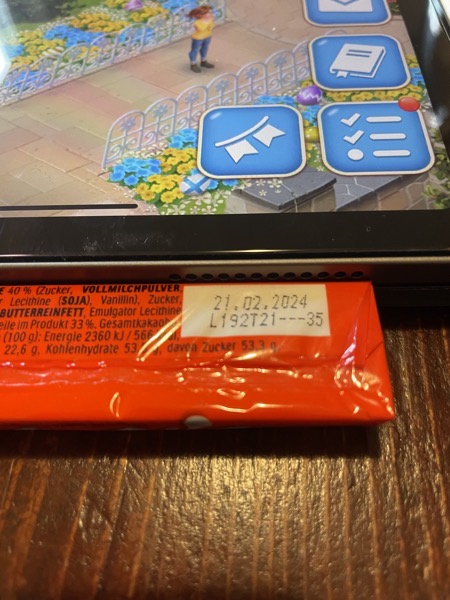 a corner of an iPad with Merge Mansion and the underside of a Kinder bar showing a best before date of February 2024