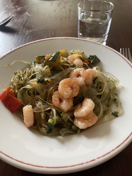 a plate of rice noodles, veggies, sprouts and shrimp with a glass of water