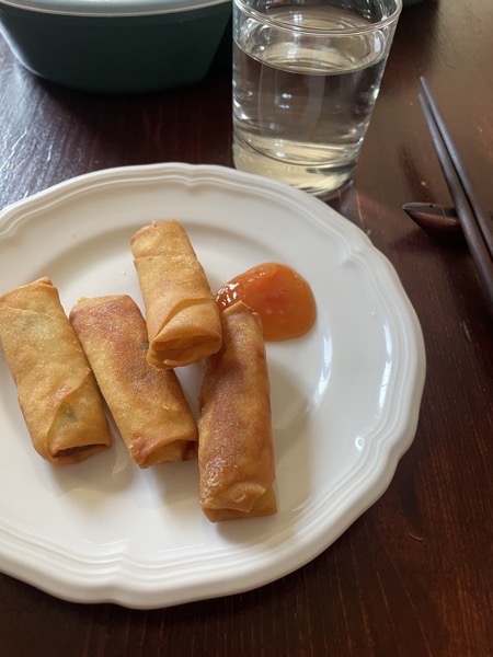 a plate with four springrolls and some sweet chili sauce, some chopsticks and a glass of water