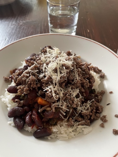 a plate of rice, red beans and ground beef with a sprinkle of parmesan and a glass of water
