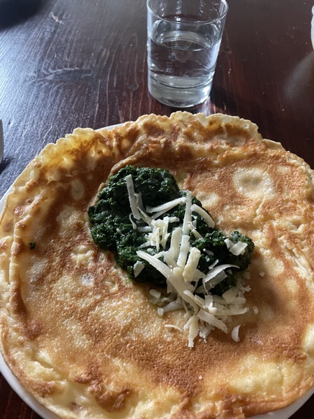 a pancake with some cooked spinach and next to it a glass of water