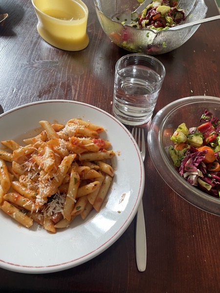 penne with tomato sauce and parmesan, a glass of water and two bowls of mixed salad