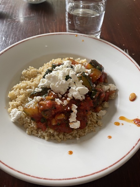 bulgur, zucchini, tomato sauce and feta with a glass of water on the side