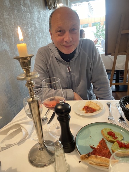 my husband sitting at a restaurant table with a piece of pizza pane and some bruschetta, a burning candle in a silver holder, a glass of rosé wine, a pepper mill and a salt shaker