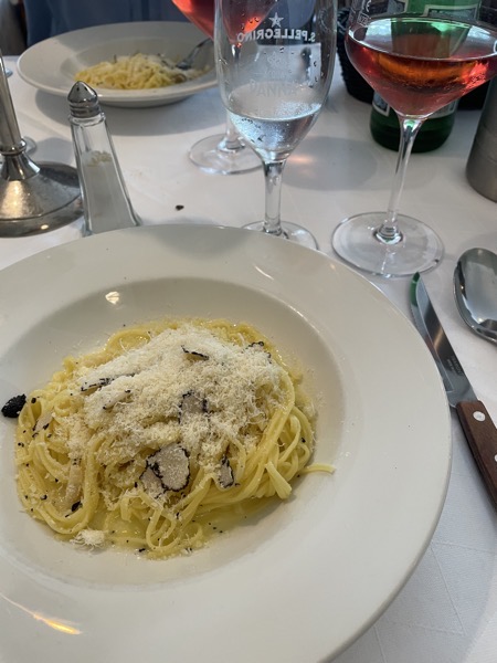 a plate of tagliolini with truffles and parmesan a glass of wine and a glass of water