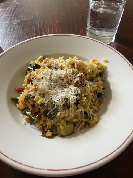 a plate of veggie, Swiss chard risotto, yellow with tumeric with grated parmesan on top and a glass of water on the side