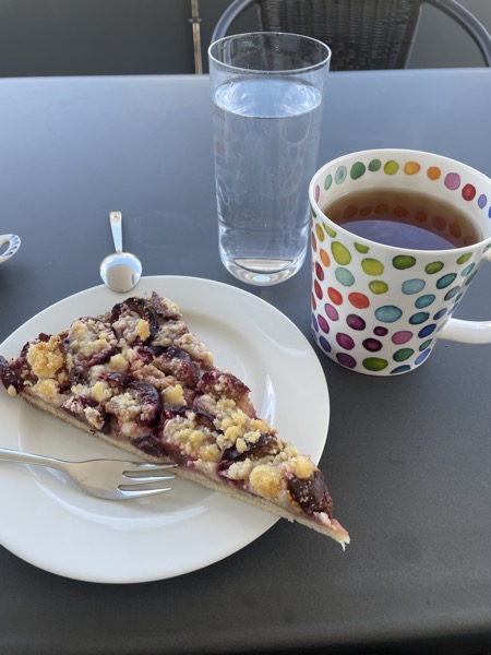 a plate of plum streusel, a big white mug with colorful dots full of tea and a glass of water