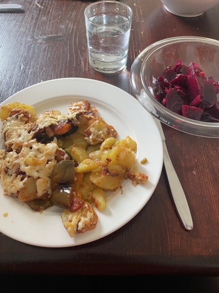 a plate with veggie and potato casserole, another with red beet salad and a glass of water