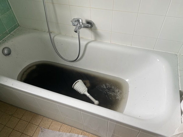 a white bathtub filled halfway with black, stinking water with a white plunger swimming in it