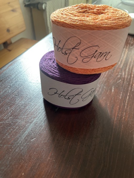 Two balls of Holst yarn, one in aubergine and the other one in clementine