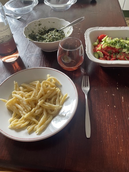 a plate of trofie, a stemless glass of rosé wine, some tomato and cucumber salad and a bowl of homemade pesto