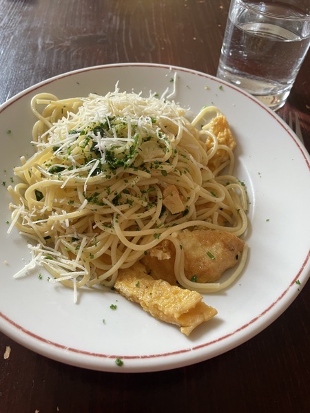 a plate of spaghetti with garlic, parsley and parmesan and pieces of omelet with a glass of water