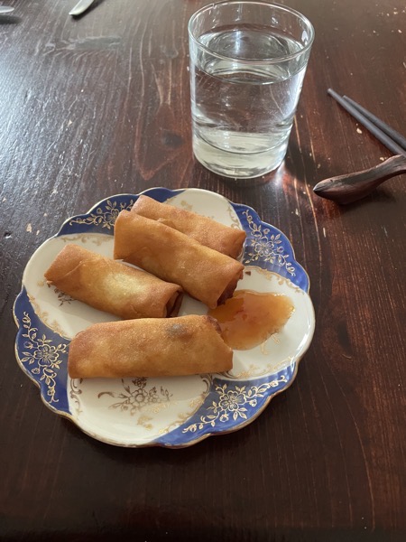 spring rolls and sweet chili sauce on a blue and cream saucer with gold detail, some chopsticks and a glass of water