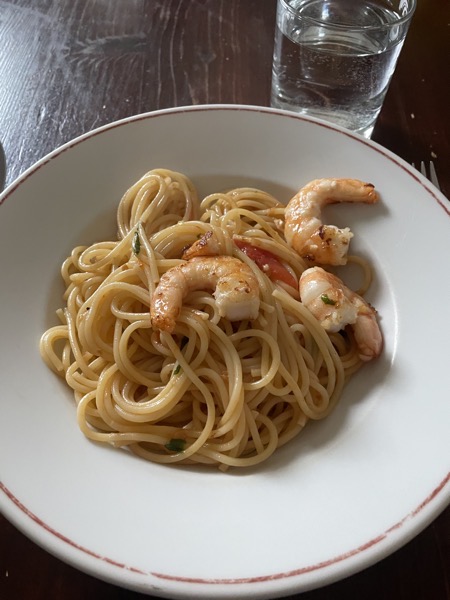 a plate of spaghetti with cherry tomatoes and shrimp with a glass of water