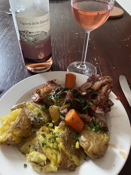 a plate of braised rabbit with potatoes and a glass of rosé wine with its bottle