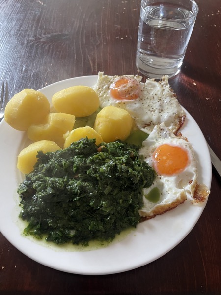 a plate of potatoes, spinach and fried eggs with a glass of water