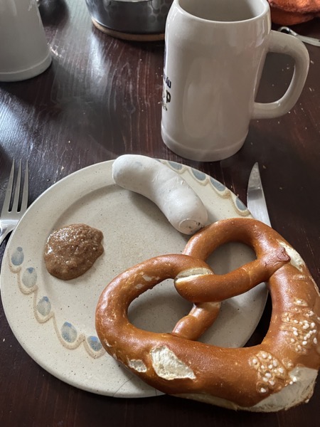 a plate with a white sausage, sweet mustard and a soft pretzel next to a stein with beer