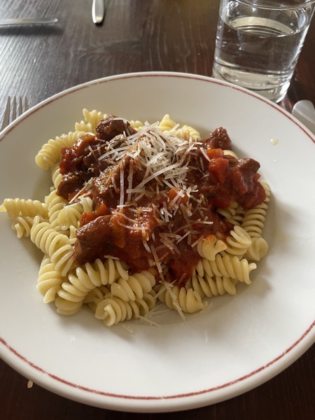 a plate of ghoulash with noodles and parmesan with a glass of water on the side