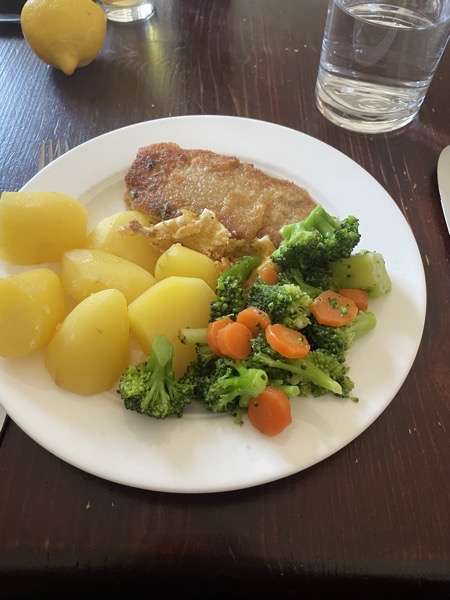 potatoes, broccoli, carrots and breaded pork cutlet with a glass of water and half a lemon in the background