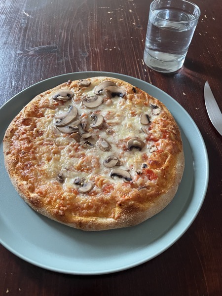 frozen mushroom pizza on a blue-green ceramic plate with a glass of water on the side