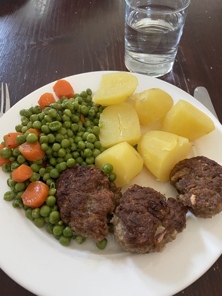 a white plate with potatoes, burgers, carrots and peas, and a glass of water