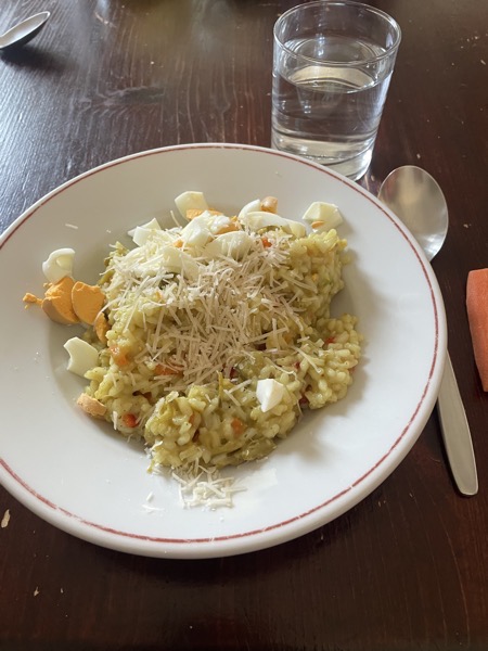 asparagus risotto with pieces of boiled egg and grated parmesan with a glass of water on the side