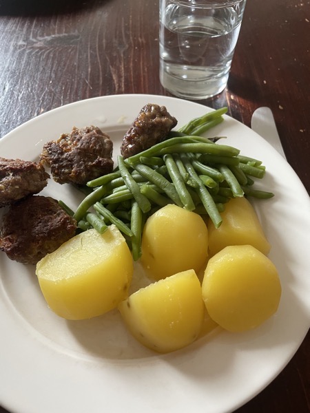 a white plate with four hamburgers, potatoes and green beans, and a glass of water