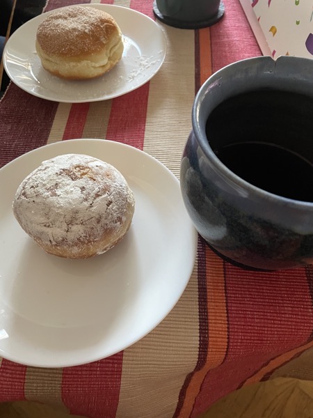 two jelly donuts on a striped tablecloth with a huge blue handthrown tea mug