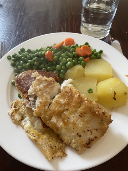 breaded fried fish filets with potatoes, green peas and carrots with a glass of water on the side