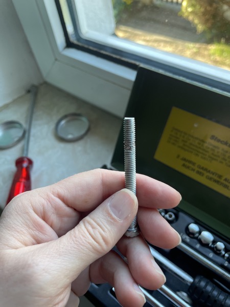 a hand holding a long screw that has a chunk missing near the end next to a window, the window sill holds a variety of screwdrivers and other tools