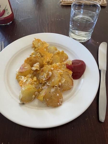 a small portion of fried potatoes with egg, a glugg of ketchup and a glass of water