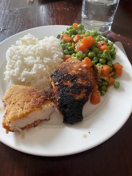 Rice, peas and carrots and some breaded chicken breast. One piece of chicken is pretty burnt. Next to the plate is a glass of water
