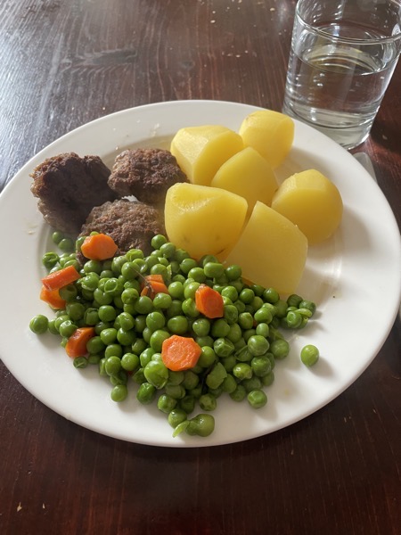 burgers, potatoes, peas and carrots with a glass of water on the side