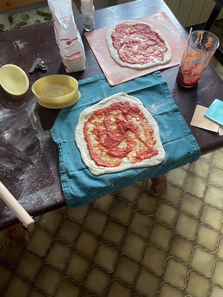rather square raw pizzas with tomato sauce on a messy table full of flour