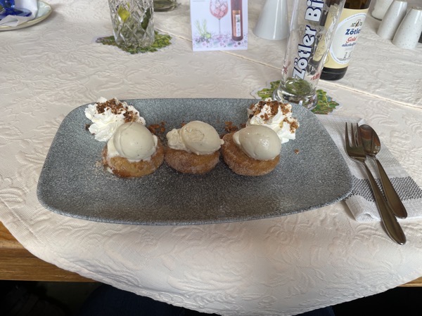 a bluish gray rectangular plate with three apple fritters, each with a scoop of ice cream on the top and  some whipped cream swirls