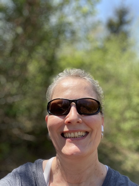 Susanne in sunglasses in front of green trees