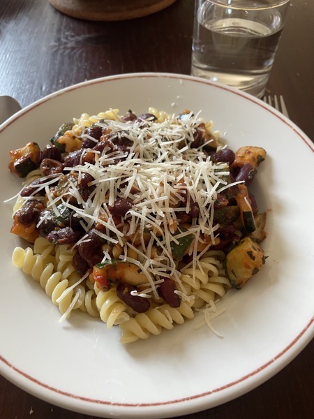 a plate of girandole with veggies, kidney beans and grated cheese and a glass of water on the side