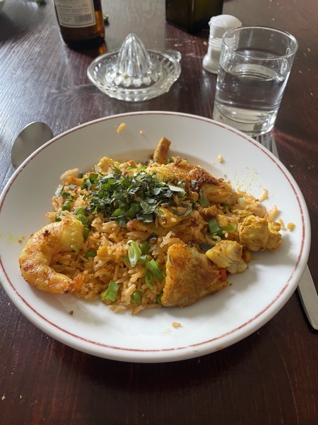 saffron rice with bits of chicken breast, fish and shrimp and a glass of water on a cluttered table with bottles, a citrus press and a salt shaker